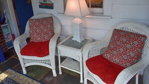 Two wicker chairs with red cushions and a white table with a lamp between them. - Lovely 3 bedroom ranch home well maintained by owners (Dennis Port)