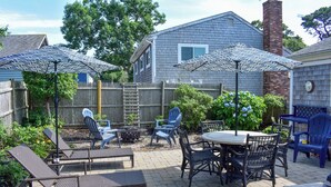 A patio with outdoor furniture, including lounge chairs and a table, surrounded by a wooden fence and greenery. - Lovely 3 bedroom ranch home well maintained by owners (Dennis Port)
