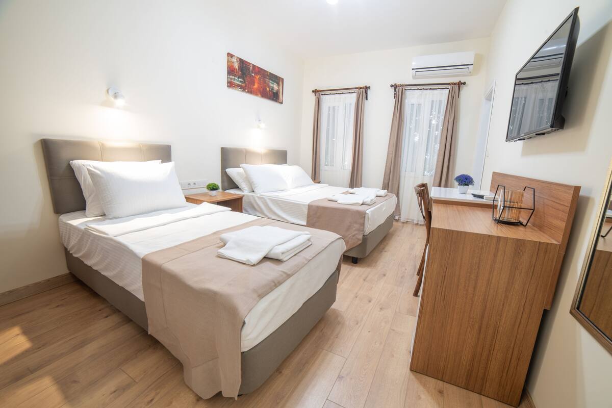 Habitación de hotel con dos camas, un escritorio, una silla, un televisor y un equipo de aire acondicionado.