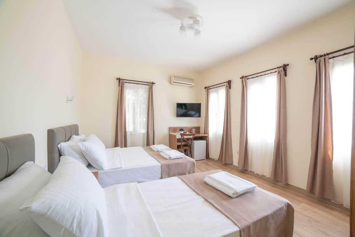Habitación de hotel con dos camas, un escritorio, una silla, un televisor y un aire acondicionado.