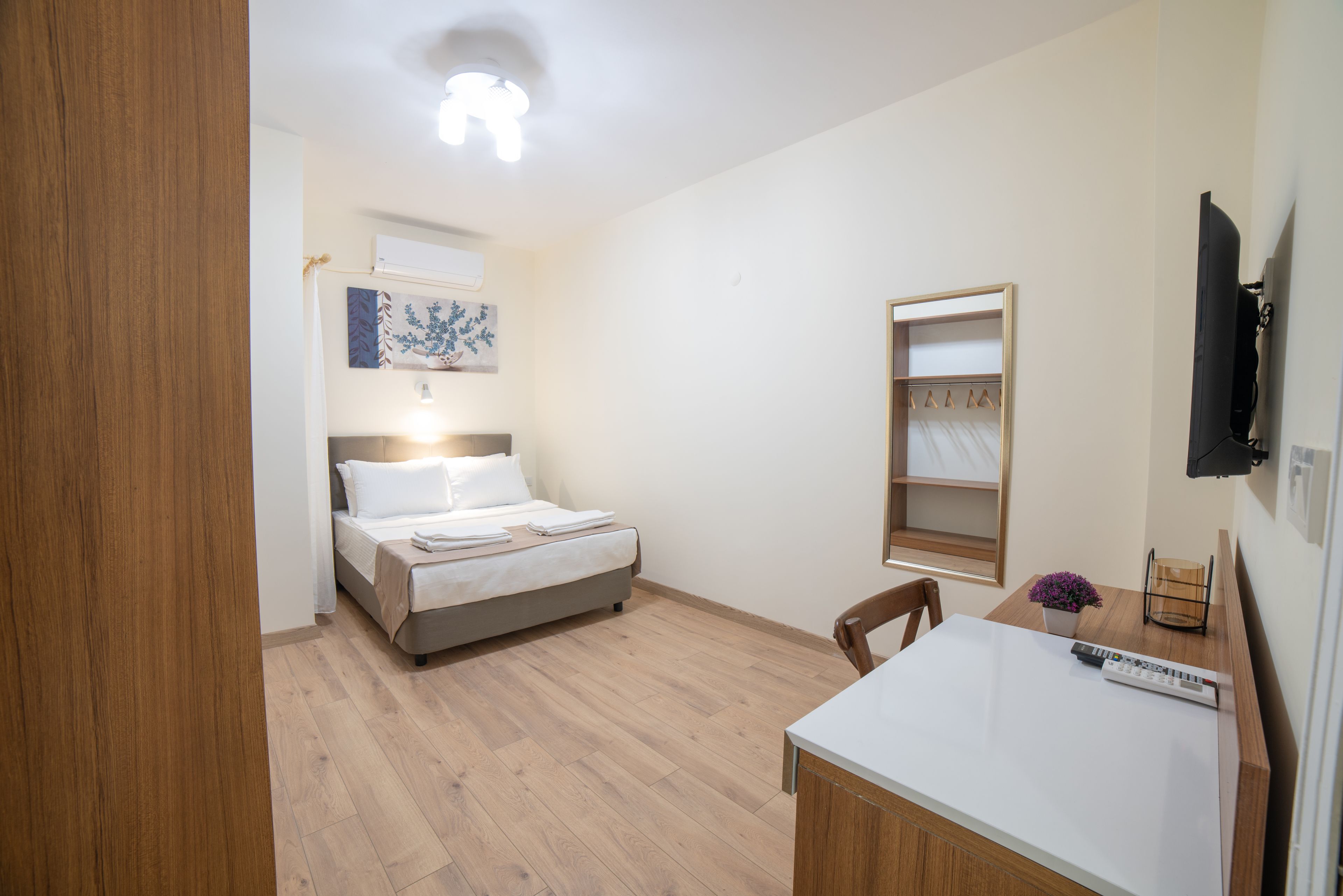 A bedroom with a bed, bedside table, chair, and a TV mounted on the wall.