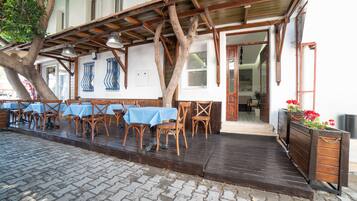 An outdoor seating area with wooden tables and chairs, a wooden deck, and a building entrance.