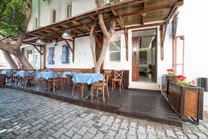 An outdoor seating area with wooden tables and chairs, a wooden deck, and a building entrance.