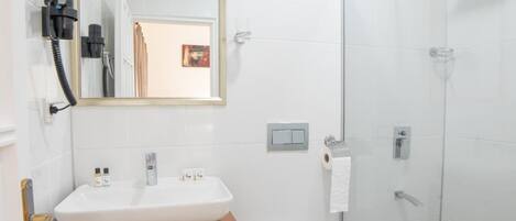 A modern bathroom with a white sink, wooden vanity, a glass shower enclosure, and a mirror above the sink.