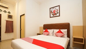 A hotel room with a bed, a headboard, a wall-mounted picture, and a small wooden nightstand.