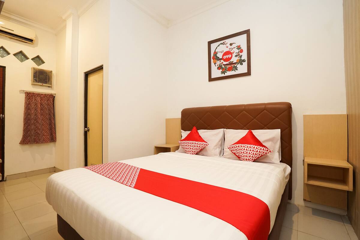 A hotel room with a bed, a headboard, a wall-mounted picture, and a small wooden nightstand.