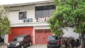 A building with a large red garage door, a black car parked in front, and several motorcycles parked outside.