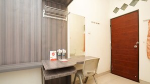 A small room with a wooden door, a tiled floor, a desk with a chair, and a towel rack.