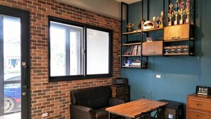 A room with a brick wall, a large window, a sofa, a wooden table, a TV, and shelves with trophies. - Letes stay (Shoufeng)