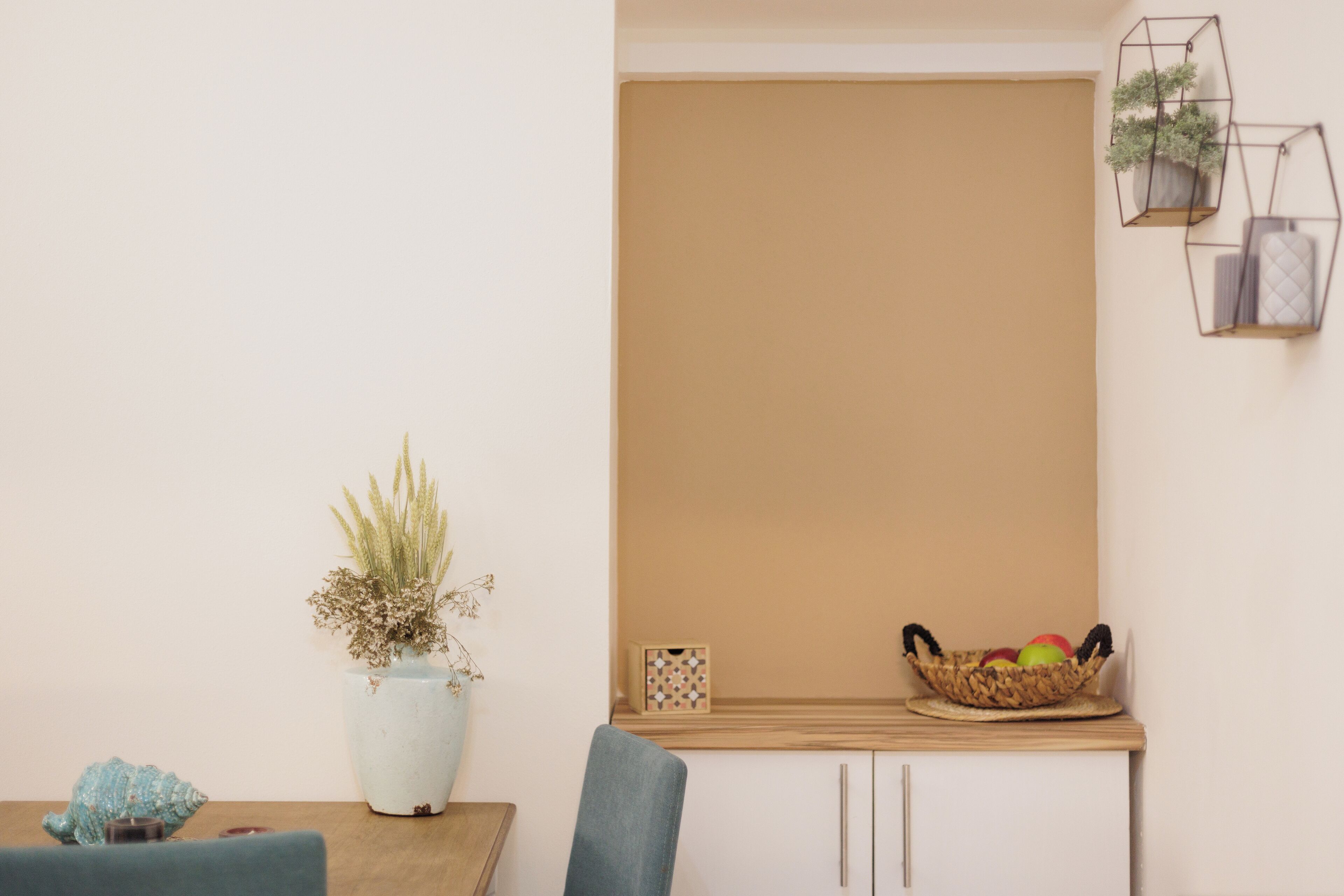 Comedor con mesa, sillas, planta en maceta, frutero y lámpara de pared.