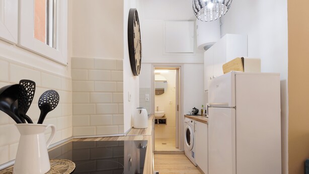 Une cuisine étroite avec un plan de travail noir, un réfrigérateur blanc et un lave-linge.