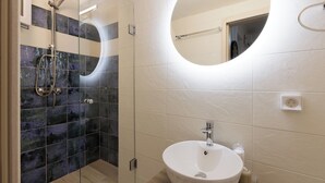 Une salle de bain moderne avec une douche à parois de verre, un miroir rond et un lavabo blanc.