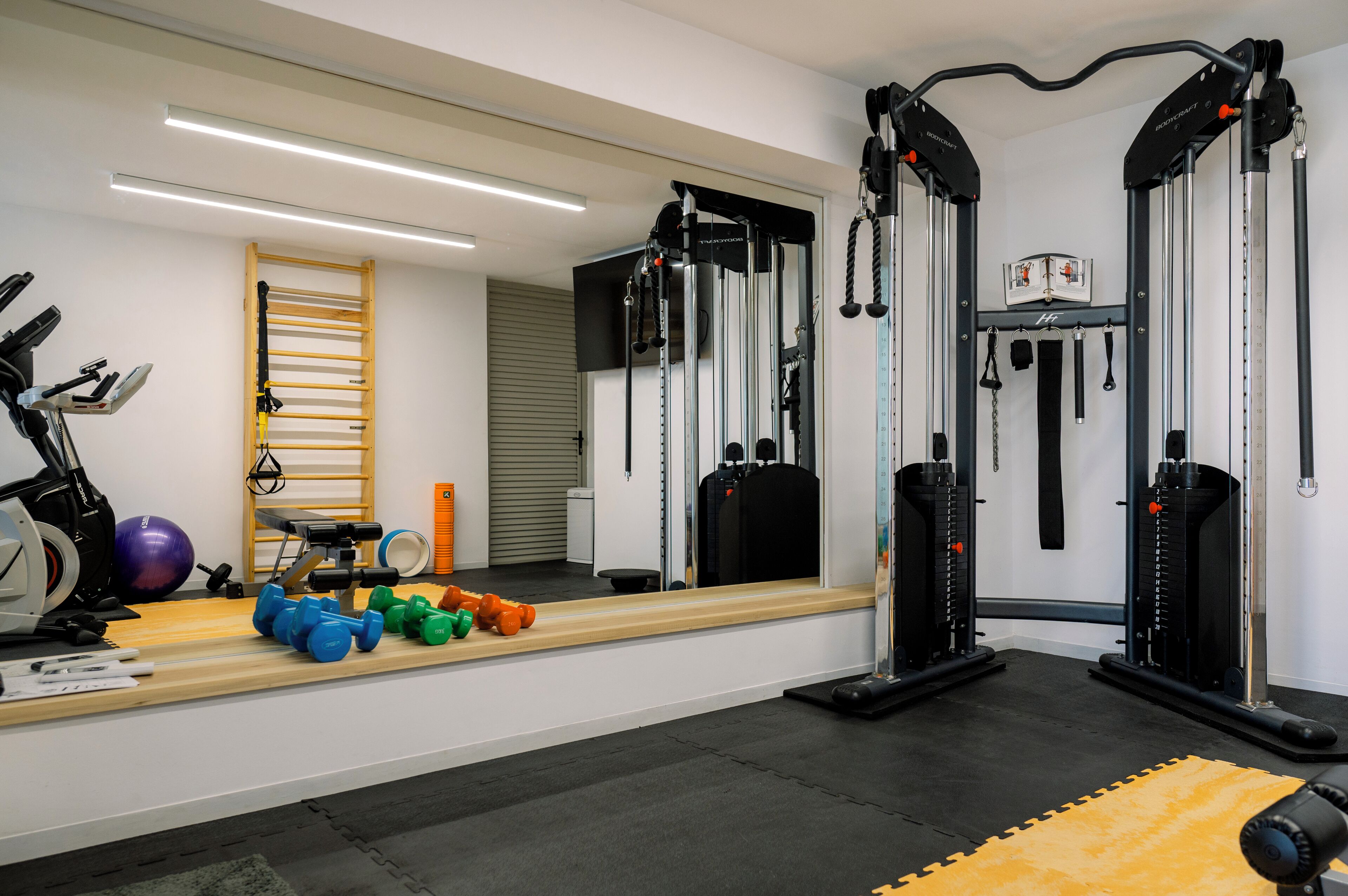 Ein Fitnessraum mit Trainingsgeräten, einem Spiegel und einer Holzlaufleiter.
