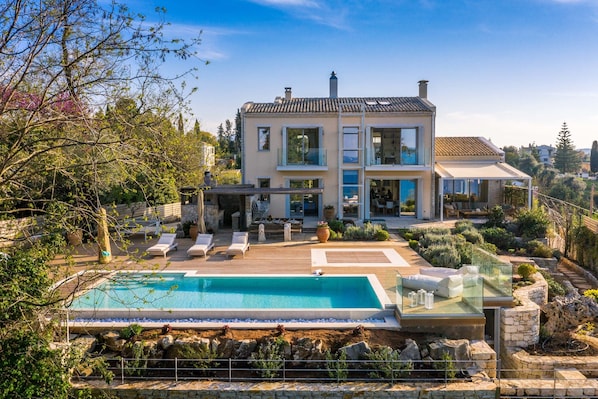 A two-story house with a swimming pool, outdoor seating, and a garden.