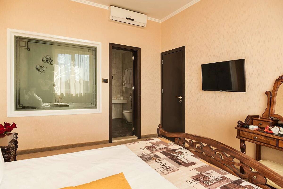 A bedroom with a bed, a TV, a wooden dresser, and a bathroom door.