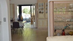 A dining area with a table and chairs, a kitchen with cabinets, and a glass display case with items. - La Villa Jalna Chambres Appartement (Roquefort-les-Pins)