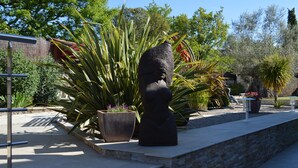 A garden with a large black statue, potted plants, and a stone wall. - La Villa Jalna Chambres Appartement (Roquefort-les-Pins)