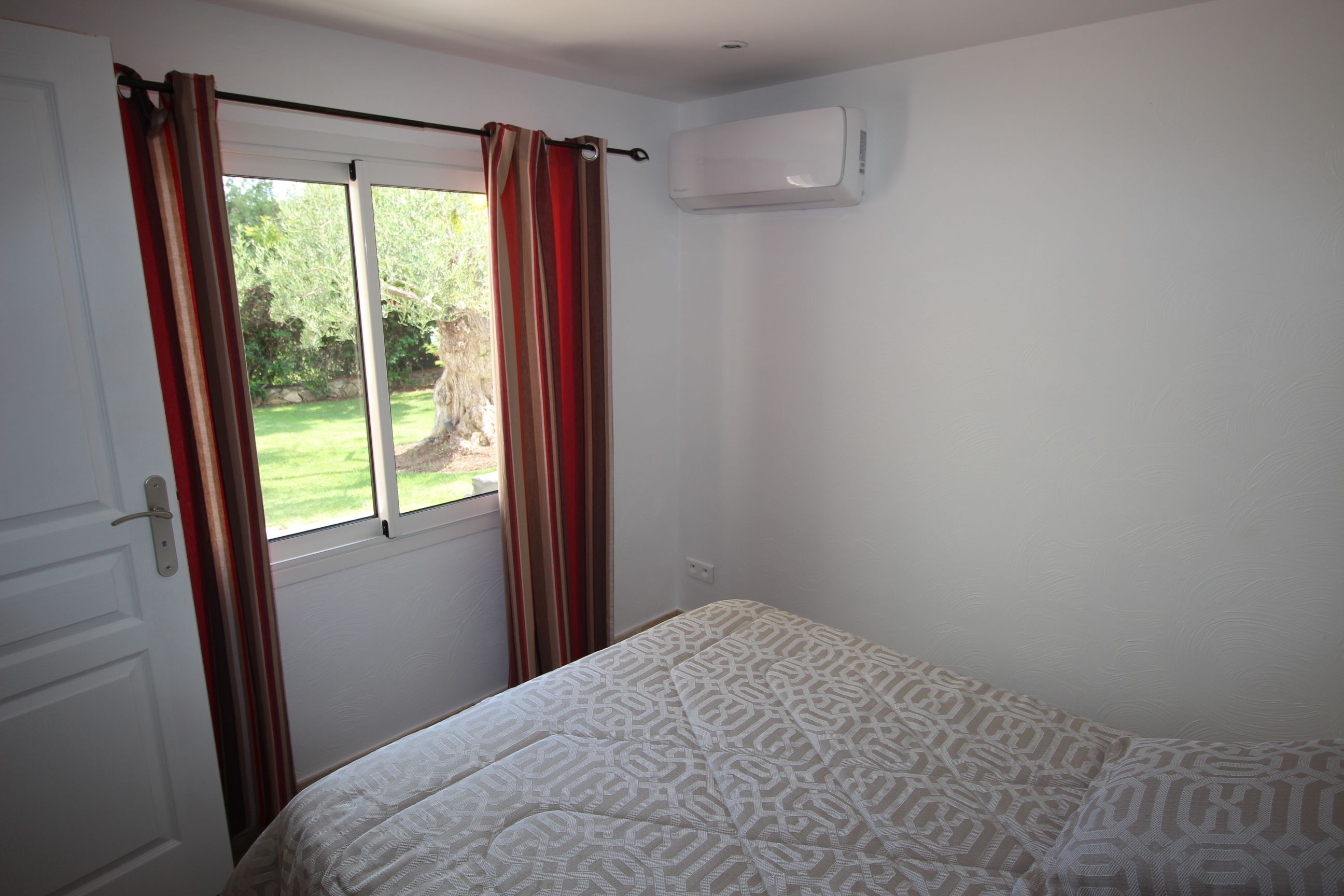 A room with a bed, a window with curtains, an air conditioning unit, and a door.
