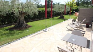 An outdoor patio with a stone floor, a table with chairs, and a small garden area with trees and a lawn. - La Villa Jalna Chambres Appartement (Roquefort-les-Pins)