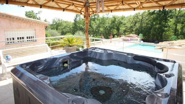 A hot tub under a bamboo roof, surrounded by a pool and greenery. - La Villa Jalna Chambres Appartement (Roquefort-les-Pins)