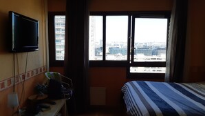 A hotel room with a bed, a television mounted on the wall, a desk with a lamp, and a window offering a city view. - PARIS_BNF Economical, comfortable studio close to Bercy BNF and Jardin Plantes (Paris)