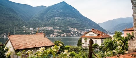A mountainous landscape with a lake, houses with red-tiled roofs, and greenery in the foreground.