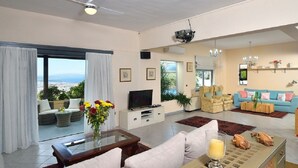 A spacious living room with a large TV, comfortable seating, a coffee table, and a view of the city.