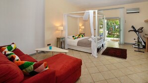 A bedroom with a four-poster bed, a red sofa, a small table, and a bike in the corner.