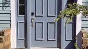 A blue double door with a doormat, a small window, and a lantern on the wall.