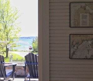 A view from a room with a window overlooking a grassy area and a body of water. There are two Adirondack chairs and a table outside. - Life Is Always Better At Lake Life Charlevoix - Golf Cart Included! (Charlevoix)