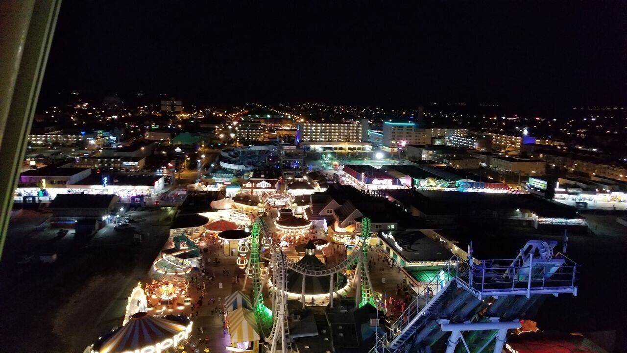 A nighttime view of a cityscape with illuminated buildings and a brightly lit amusement park area.