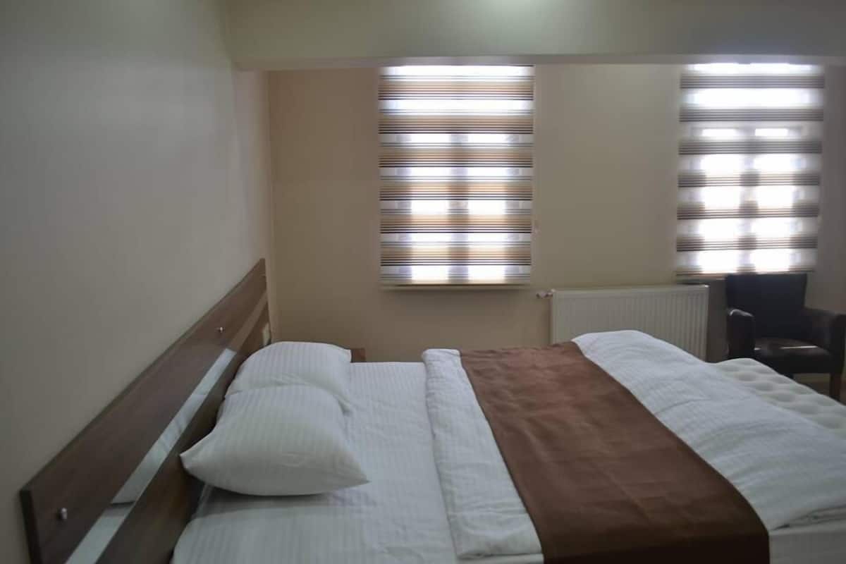 A bedroom with a bed, a window with blinds, and a chair.