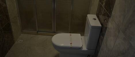 A bathroom with a toilet, a shower, and a tiled floor.