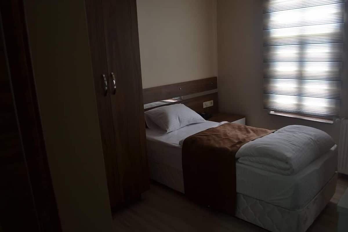 A bedroom with a bed, a nightstand, a window with blinds, and a wardrobe.