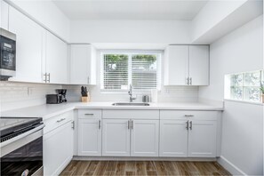 Une cuisine moderne avec des meubles blancs, un four encastré et une fenêtre équipée de stores.