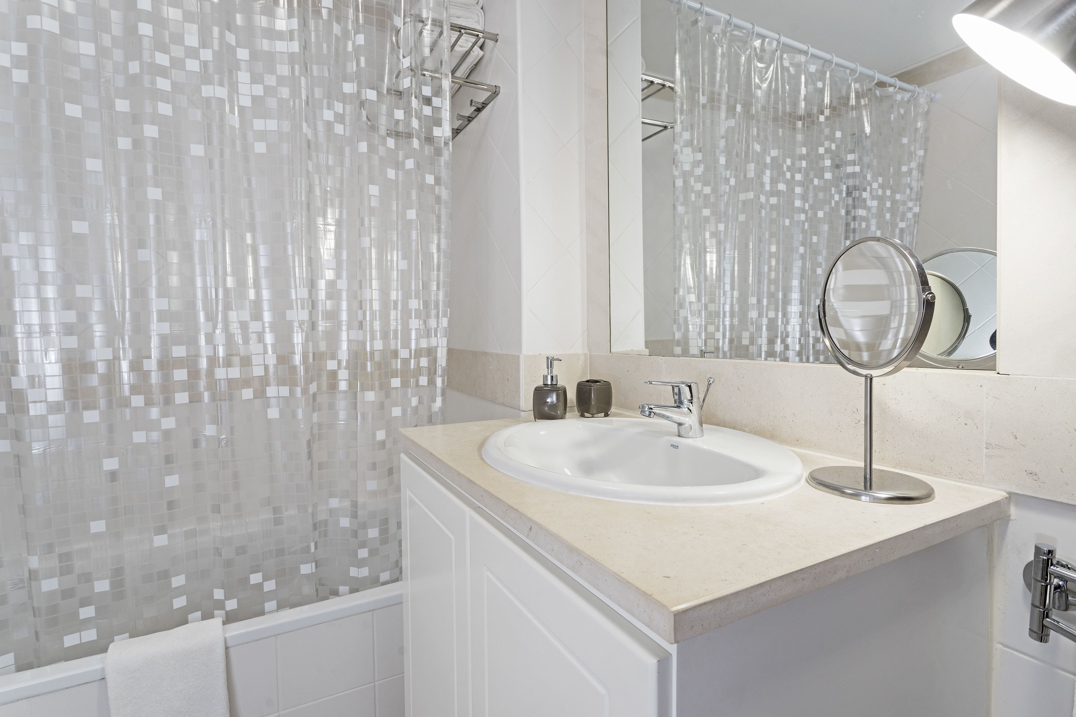Une salle de bain moderne avec un lavabo blanc, un miroir et un rideau de douche orné d’un motif en mosaïque.