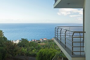 A balcony with a metal railing overlooking a coastal area with houses and a view of the sea. - 22 Caniço I By Trip2Portugal (Santa Cruz)