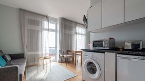 Un espace de vie compact comprenant un canapé, une table à manger avec des chaises, un lave-linge, un four à micro-ondes et un petit coin cuisine.