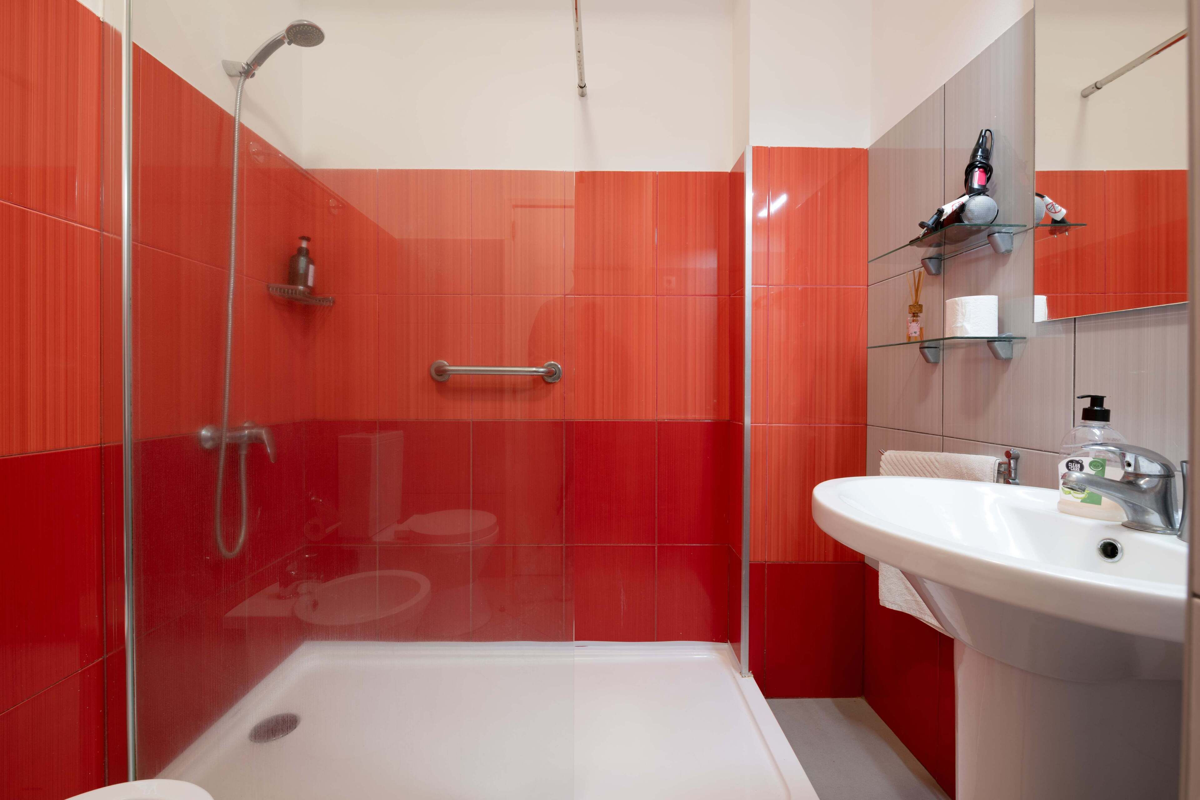 A modern bathroom with a glass-enclosed shower, a white sink, and red tiled walls.