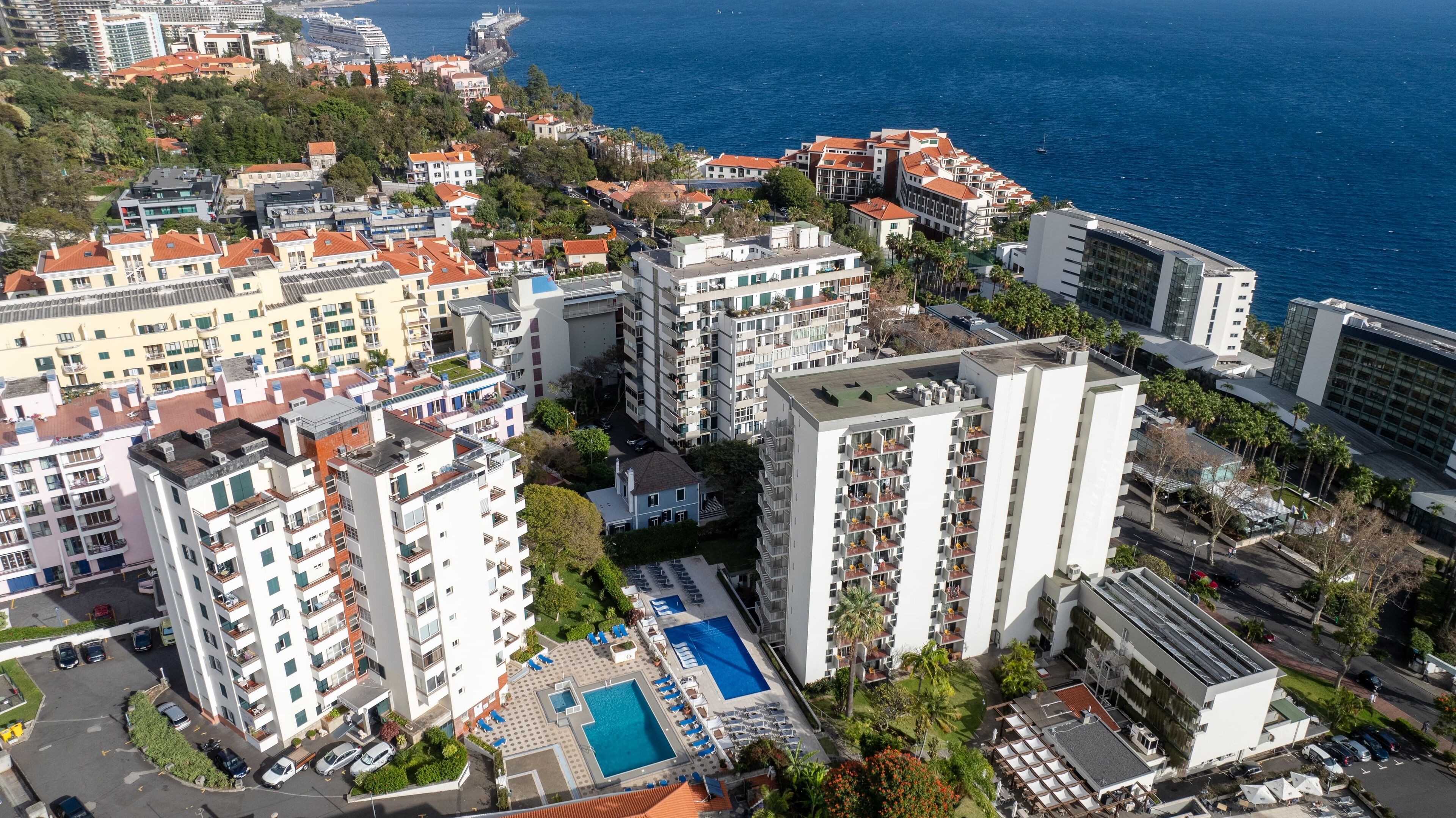 A high-rise hotel with multiple balconies, a swimming pool, and a view of the sea.