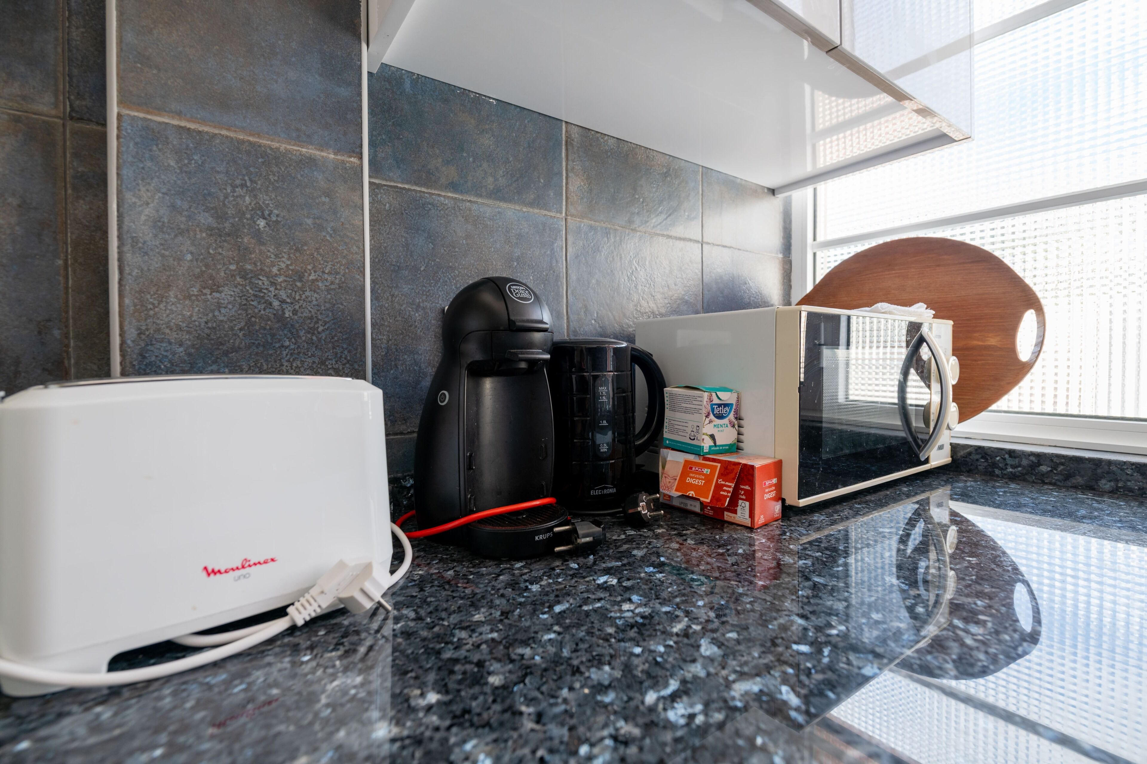 A kitchen counter with a toaster, coffee maker, microwave, and a box of cereal.