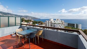 Un balcón con mesa y sillas, con vistas a una ciudad costera con edificios y el mar.