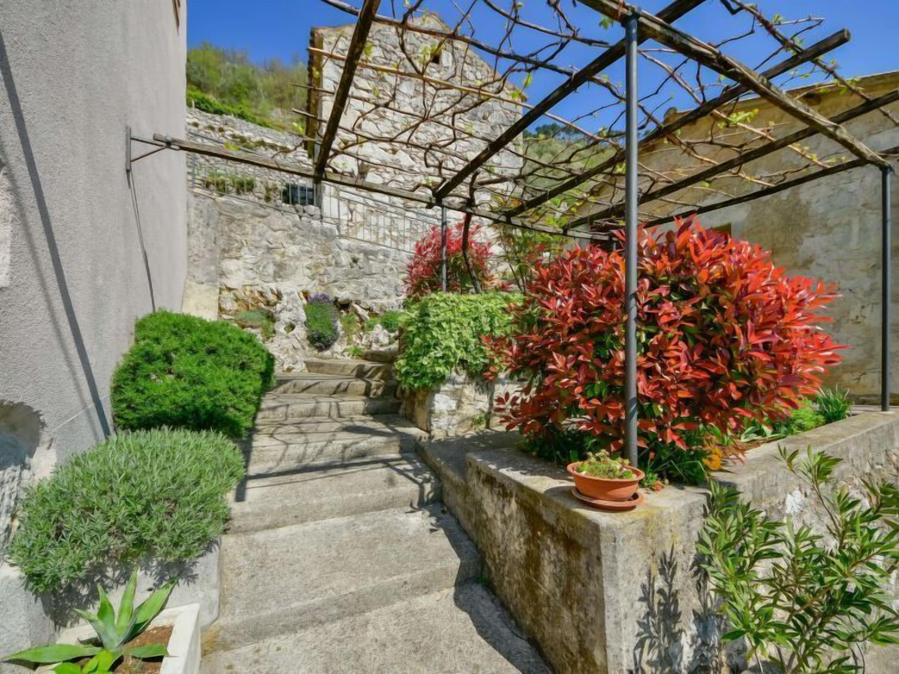 A stone staircase leading up to a stone wall with a pergola structure above.