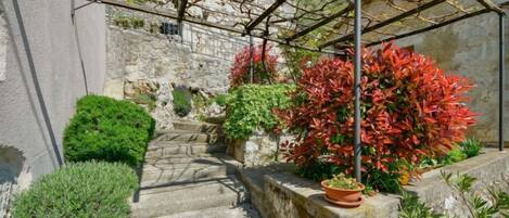 A stone staircase leading up to a stone wall with a pergola structure above.
