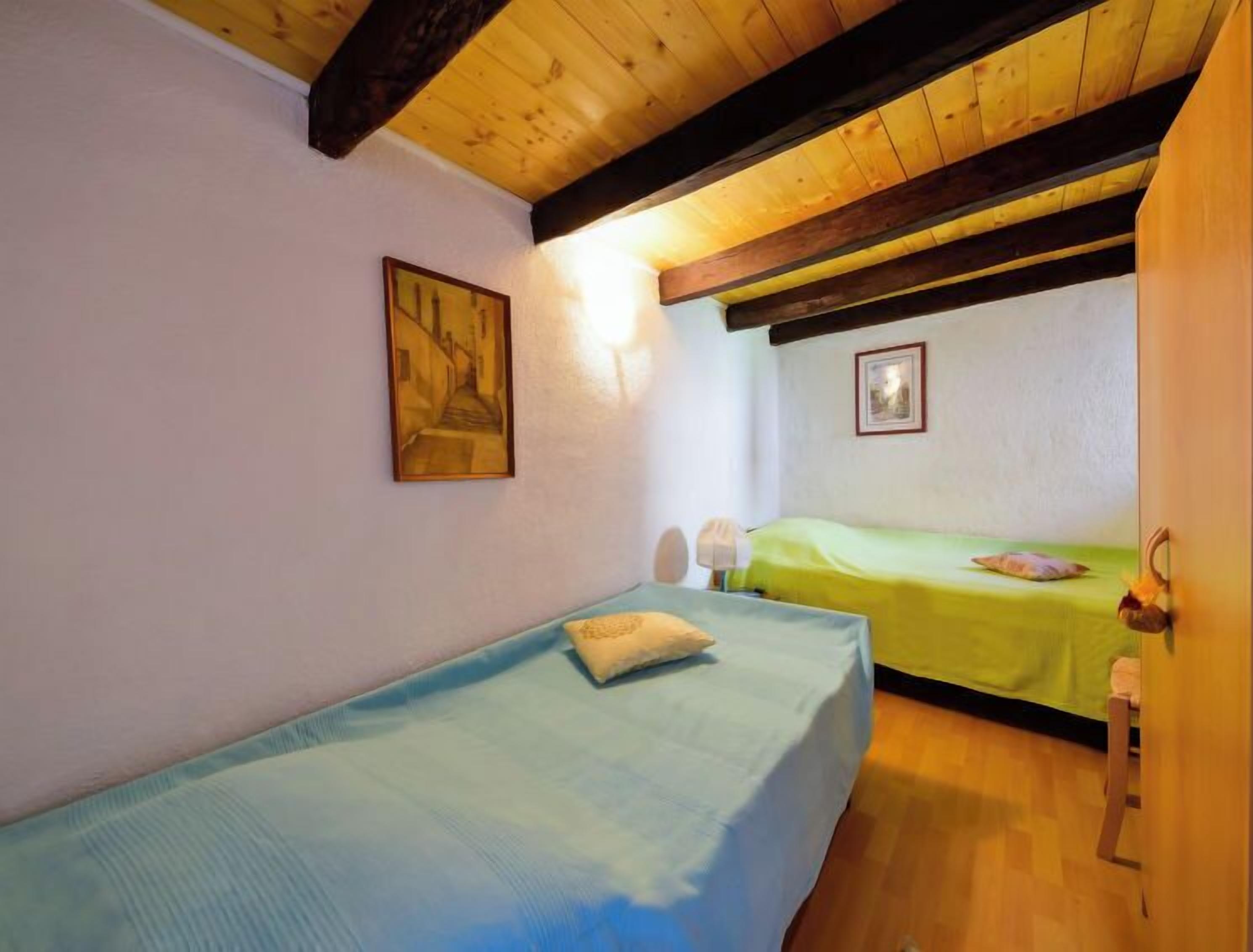 A room with two beds, wooden beams on the ceiling, and two framed pictures on the walls.