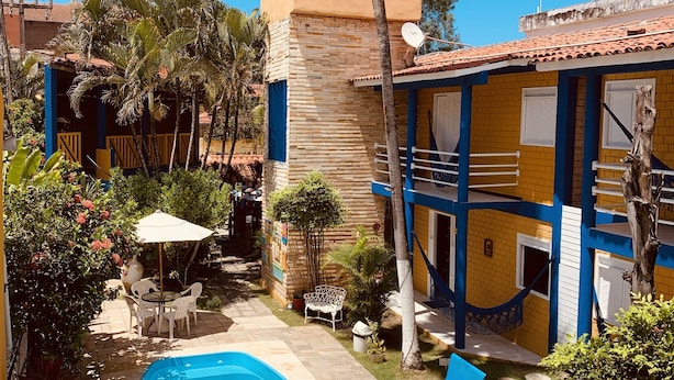 A pool area with a blue pool, white umbrellas, and a small seating area with chairs and a table. - Pousada Girassol (Ipojuca)