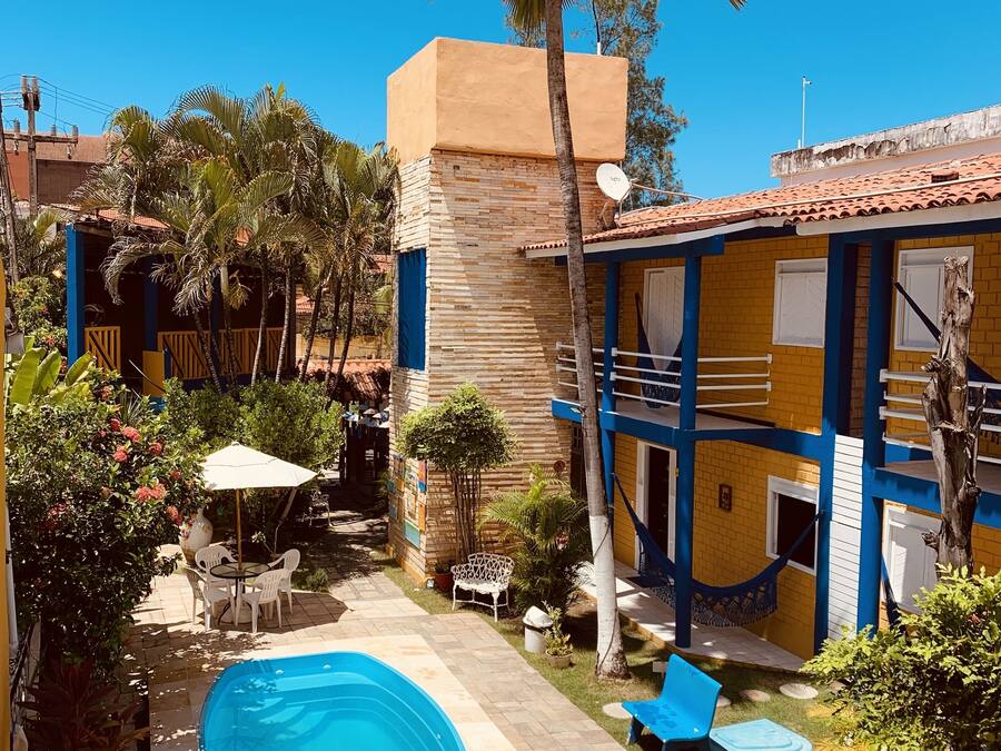 Un área de piscina con una piscina azul, sombrillas blancas y un espacio de descanso con sillas y una mesa.