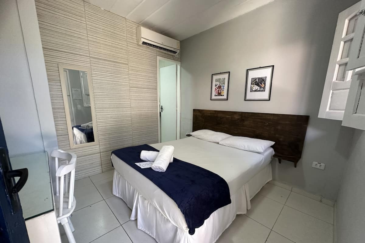 Habitación de hotel con cama, una silla, un espejo y dos cuadros en la pared.