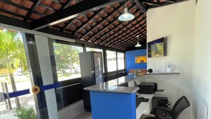 A reception area with a blue counter, black office chairs, a TV on the wall, and a ceiling with exposed beams. - Pousada Girassol (Ipojuca)
