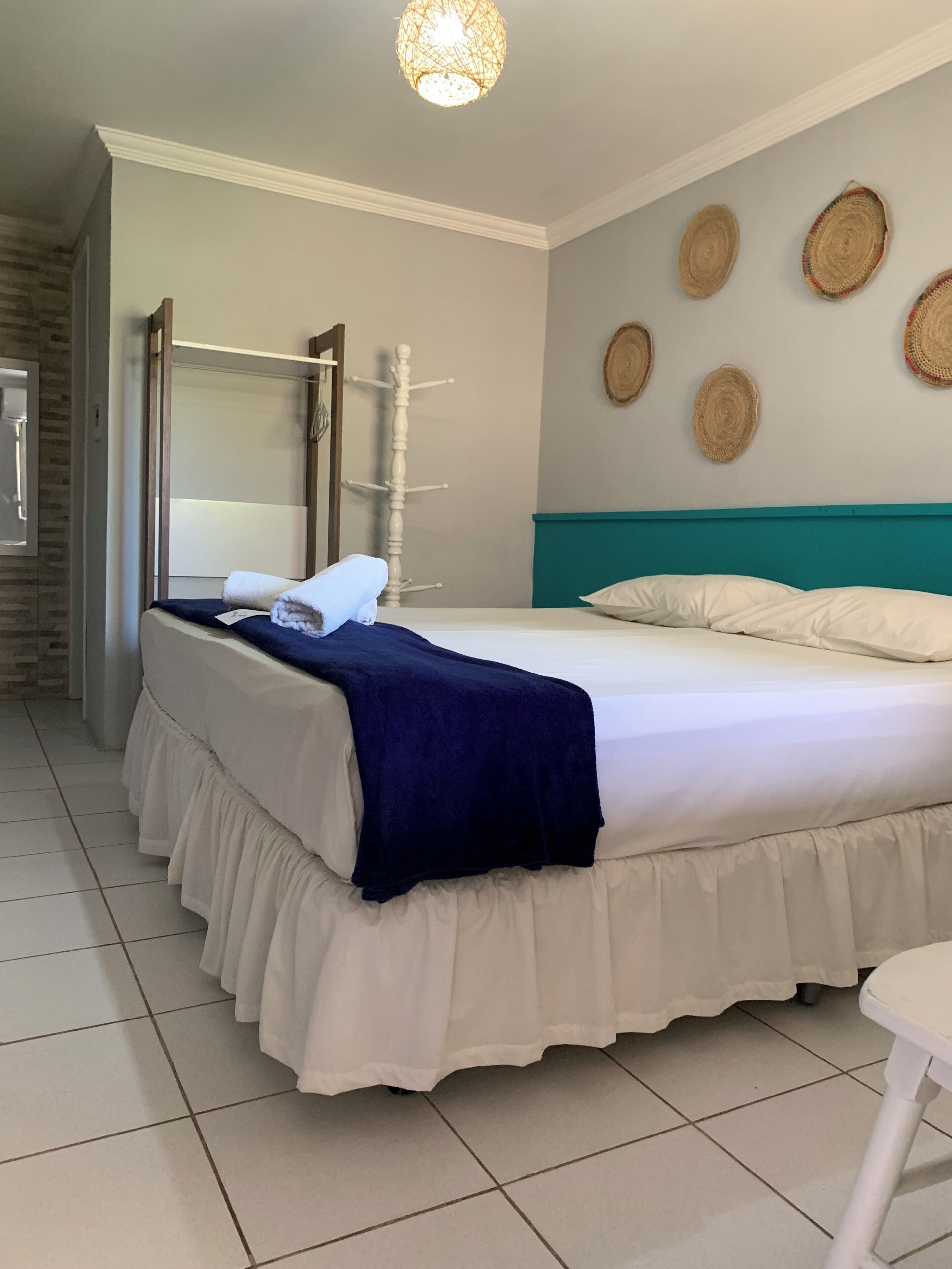 A neatly made bed with a white and blue bedspread, a wooden coat rack, and a wall with woven wall art.
